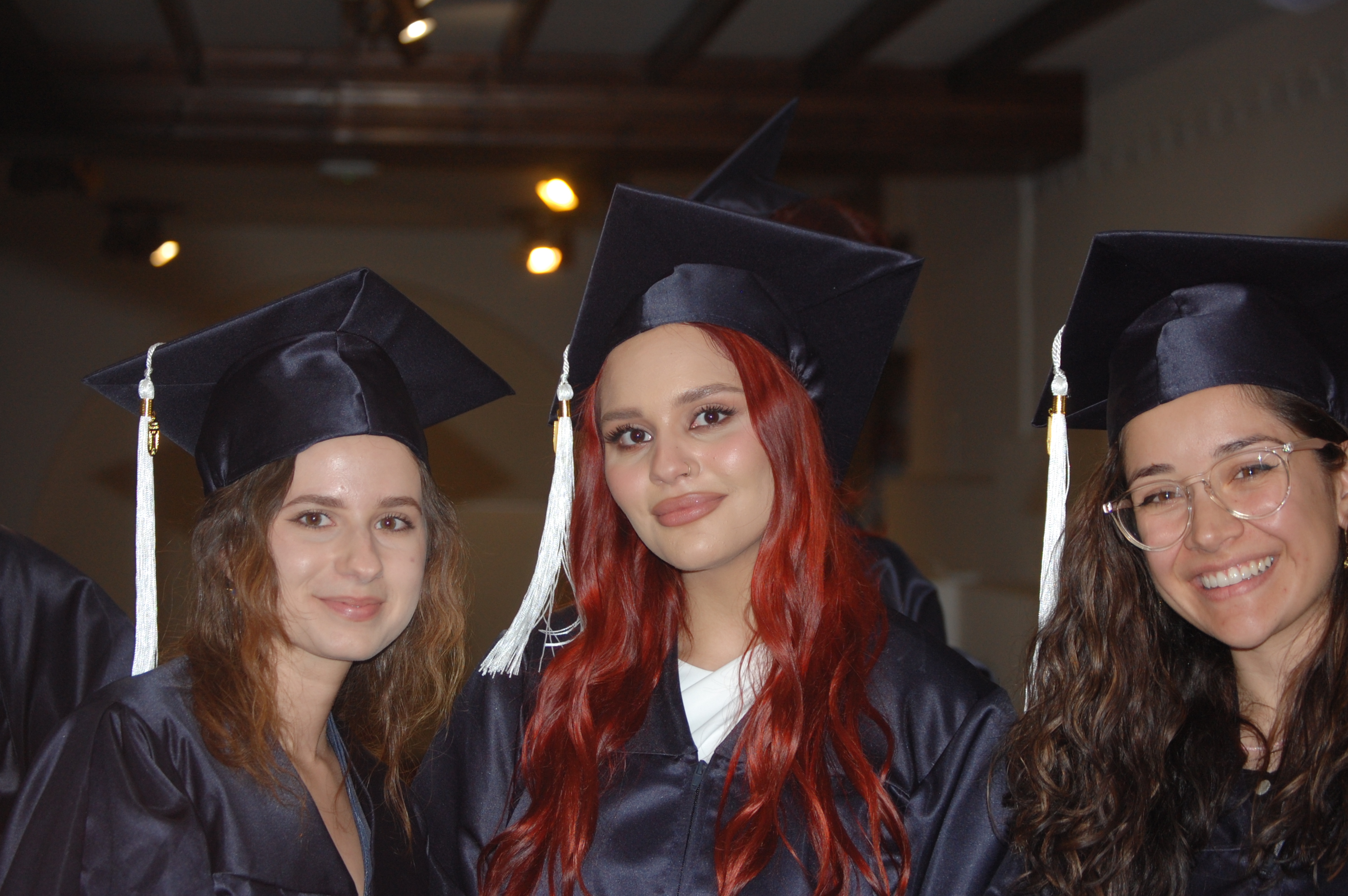 Three students dress in cap and gown for Commencement in Athens, smiling toward camera. 