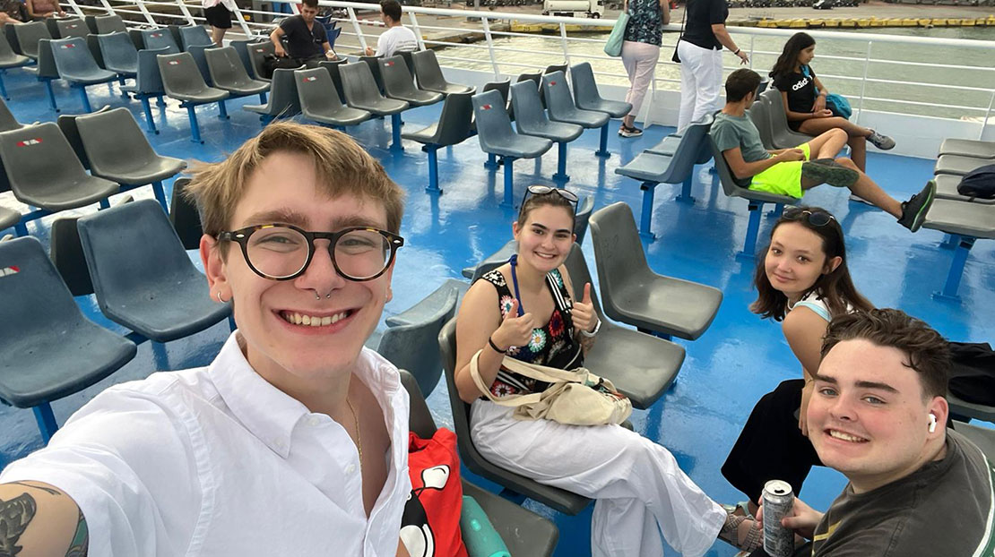 Students sitting together in blue chairs on top of cruise ship.