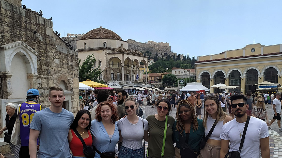 Line of students pose together with busy market with street vendors in background.