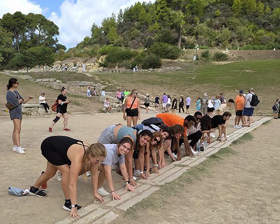 Long line of students in runners pose on stone starting line of original Olympic track.