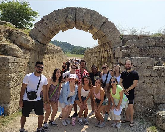 Group of students pose together between stone walls in front of ancient stone archway.