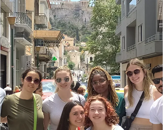 Study Abroad Student pose for a photo at Aiolou street of Athens having the Acropolis on their background 